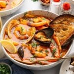 Bowl of Cioppino seafood stew with shrimp, clams, and herbs, served with toasted bread.