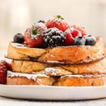 A plate of classic French toast topped with powdered sugar, strawberries, blackberries, and blueberries.