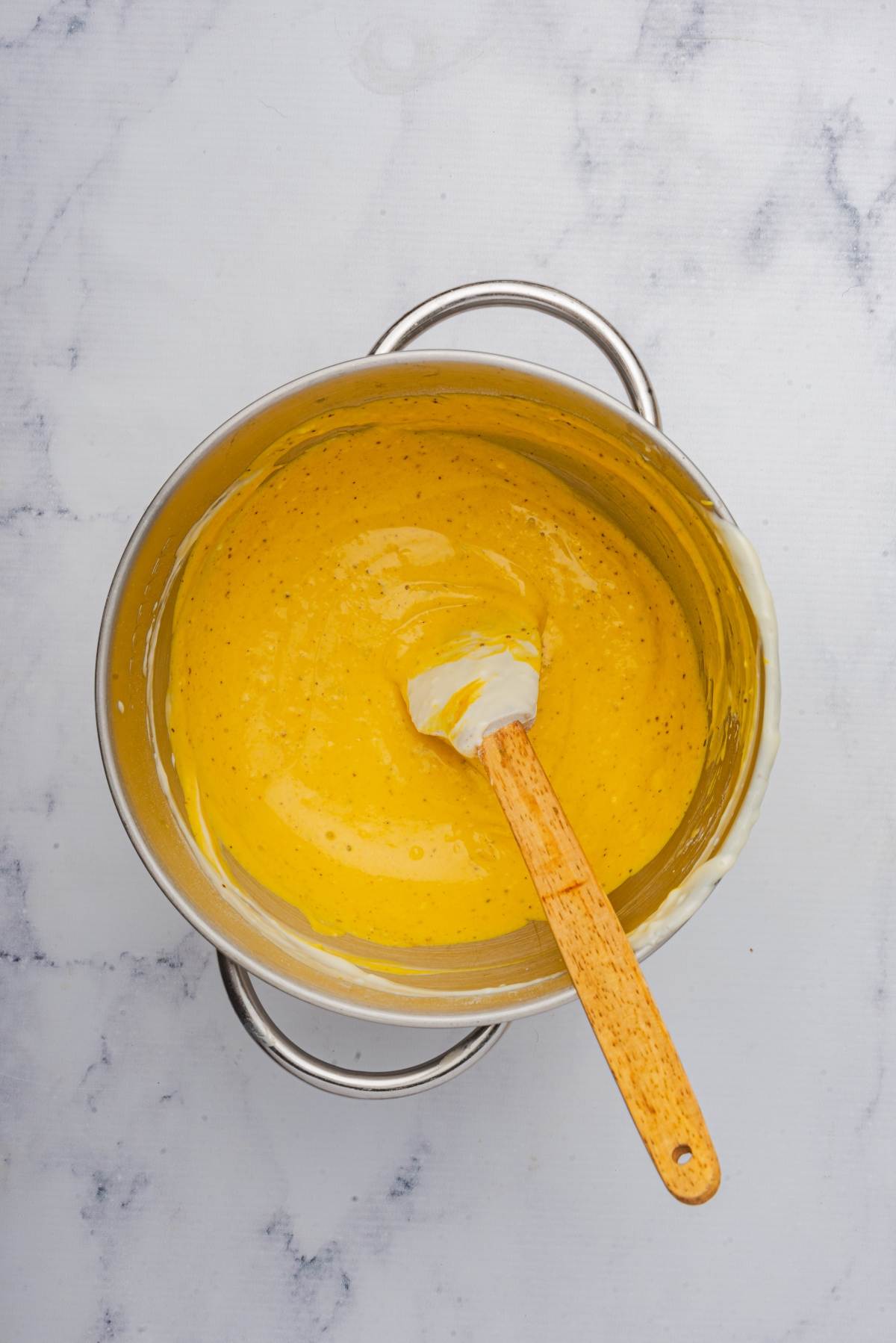 A mixing bowl filled with creamy yellow batter hints at the delight of pumpkin cheesecake bars, with a spatula resting inside. The bowl sits on a light marble surface, ready for its transformation into indulgent treats.