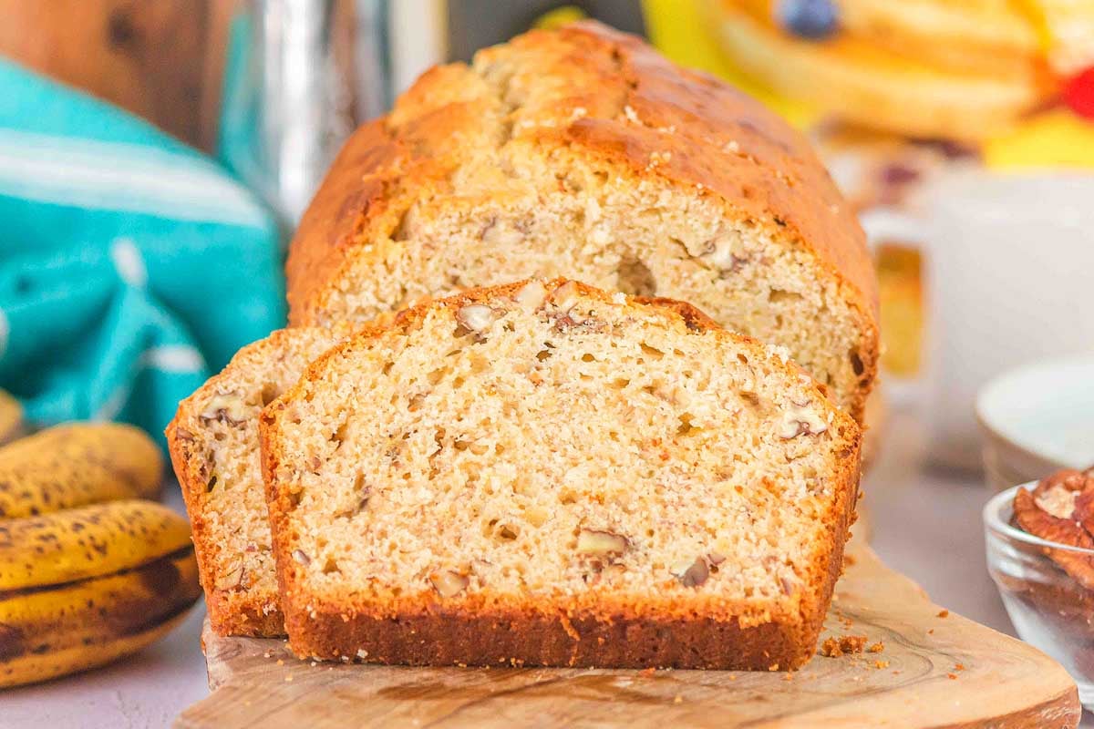 Sliced Bisquick banana bread on a wooden board with bananas and a turquoise towel in the background.