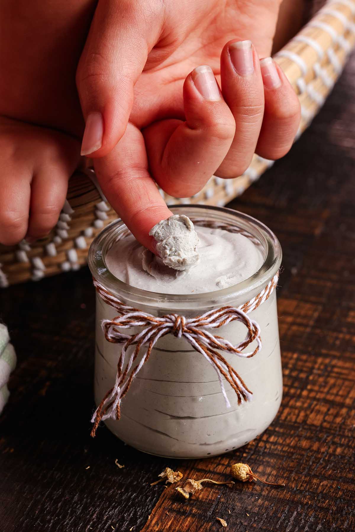 A finger taking a scoop of homemade diaper rash cream on a wooden surface.