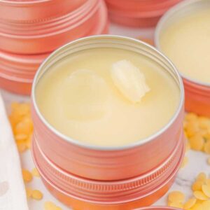 Round metal tins filled with creamy Dog Paw Balm, with yellow wax pellets scattered on a white surface.