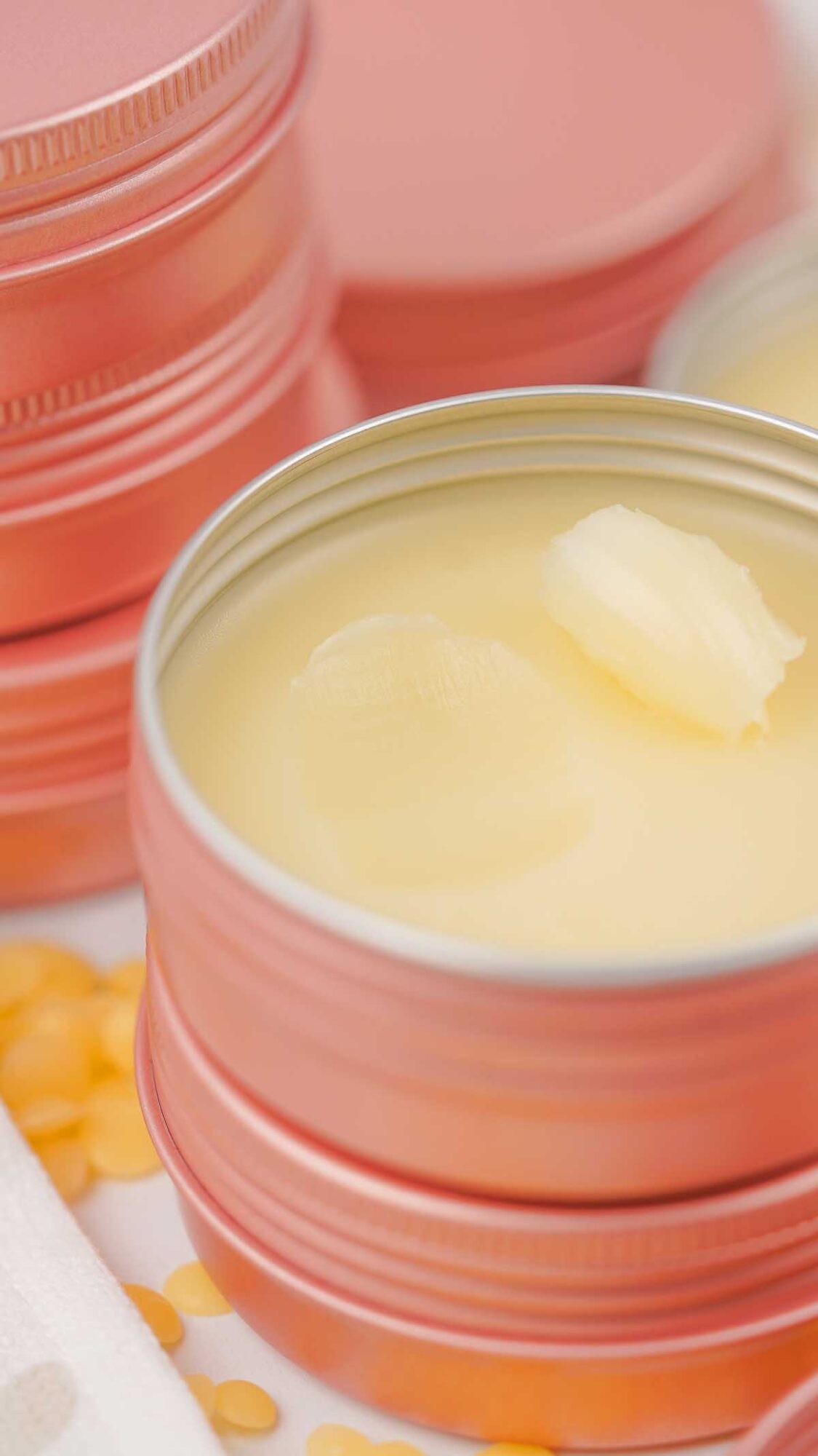 A close-up of a pink metal tin filled with Dog Paw Balm, with other tins and yellow beads in the background.