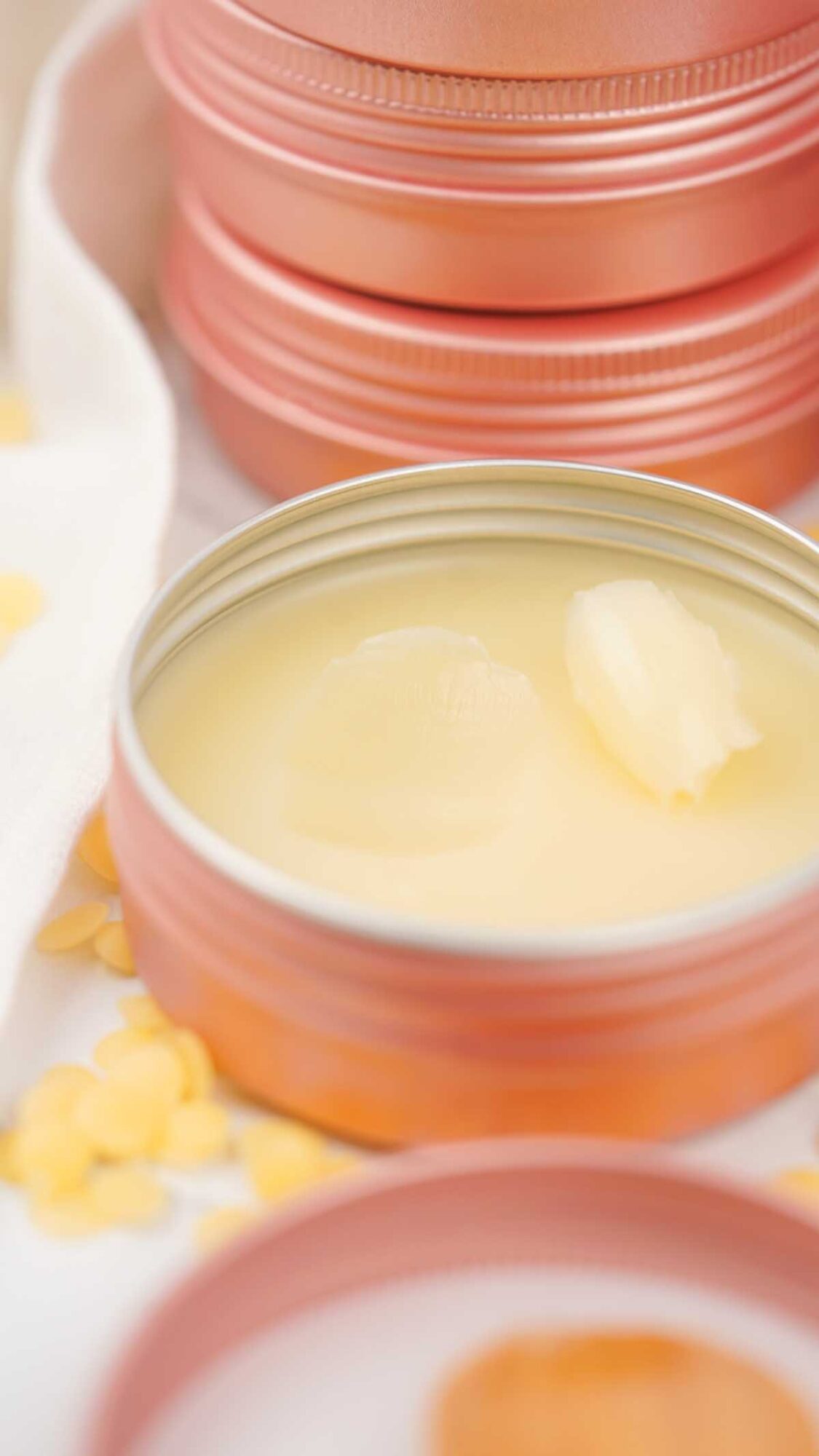 An open tin of Dog Paw Balm sits beside a few yellow wax pellets, with stacked closed tins arranged in the background.
