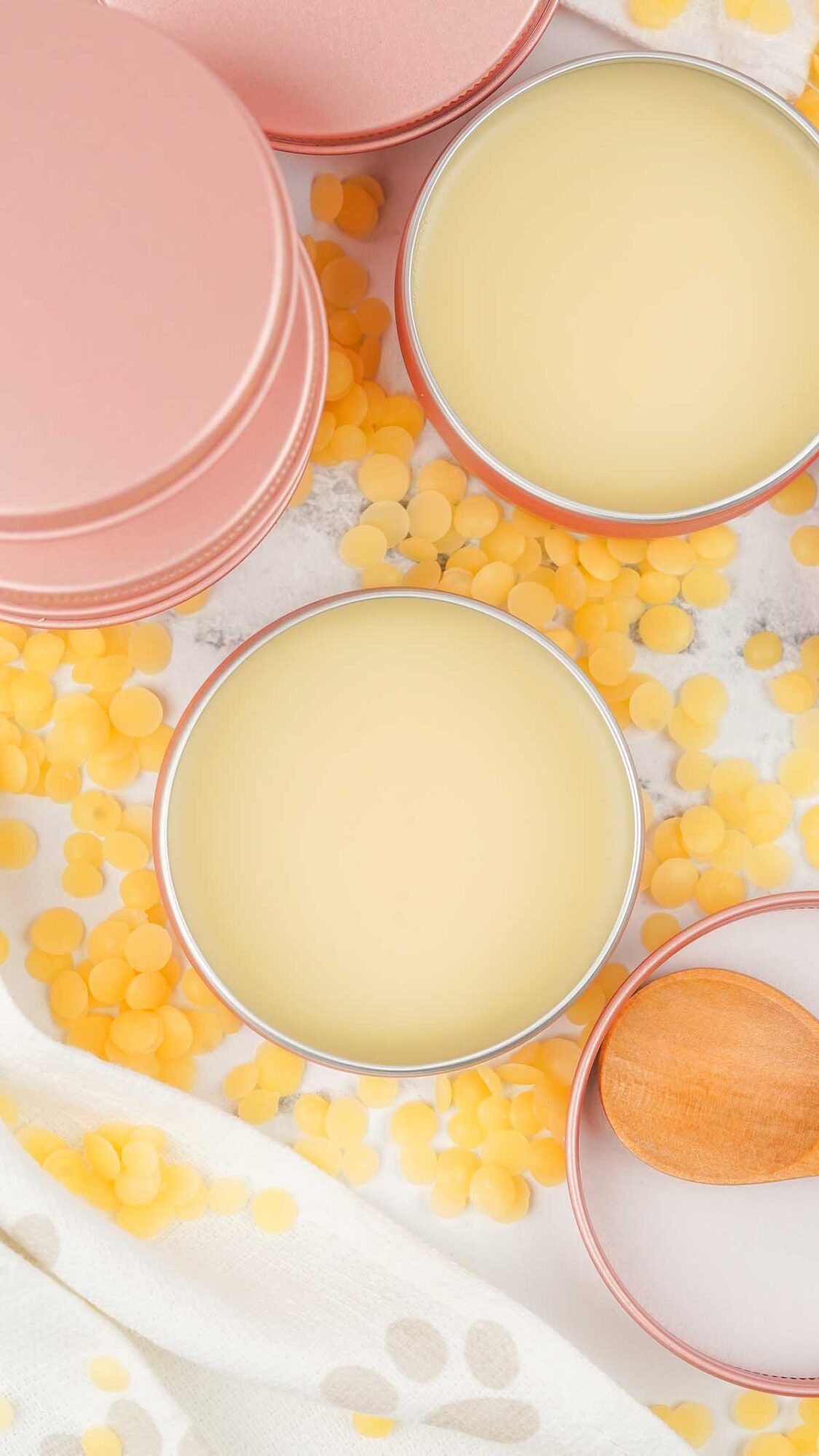 Round tins of Dog Paw Balm filled with balm, surrounded by yellow beeswax pellets and a small wooden spoon.