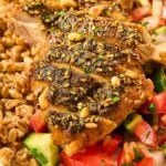 Za'atar crusted chicken breast with spices, served alongside a farro pilaf and fresh vegetable salad on a plate.