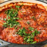 A savory pot of chicken cacciatore bubbles with rich tomato sauce, herbs, and a sprinkle of grated cheese on top.
