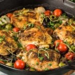 Roasted chicken Provencal with herbs, cherry tomatoes, olives, and onions in a black cast iron skillet.