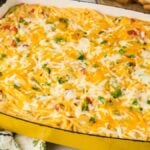 A yellow baking dish filled with chicken spaghetti casserole, topped with melted cheese and garnished with parsley.