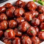 A white bowl filled with succulent slow cooker BBQ meatballs glazed with grape jelly, garnished with chopped herbs.