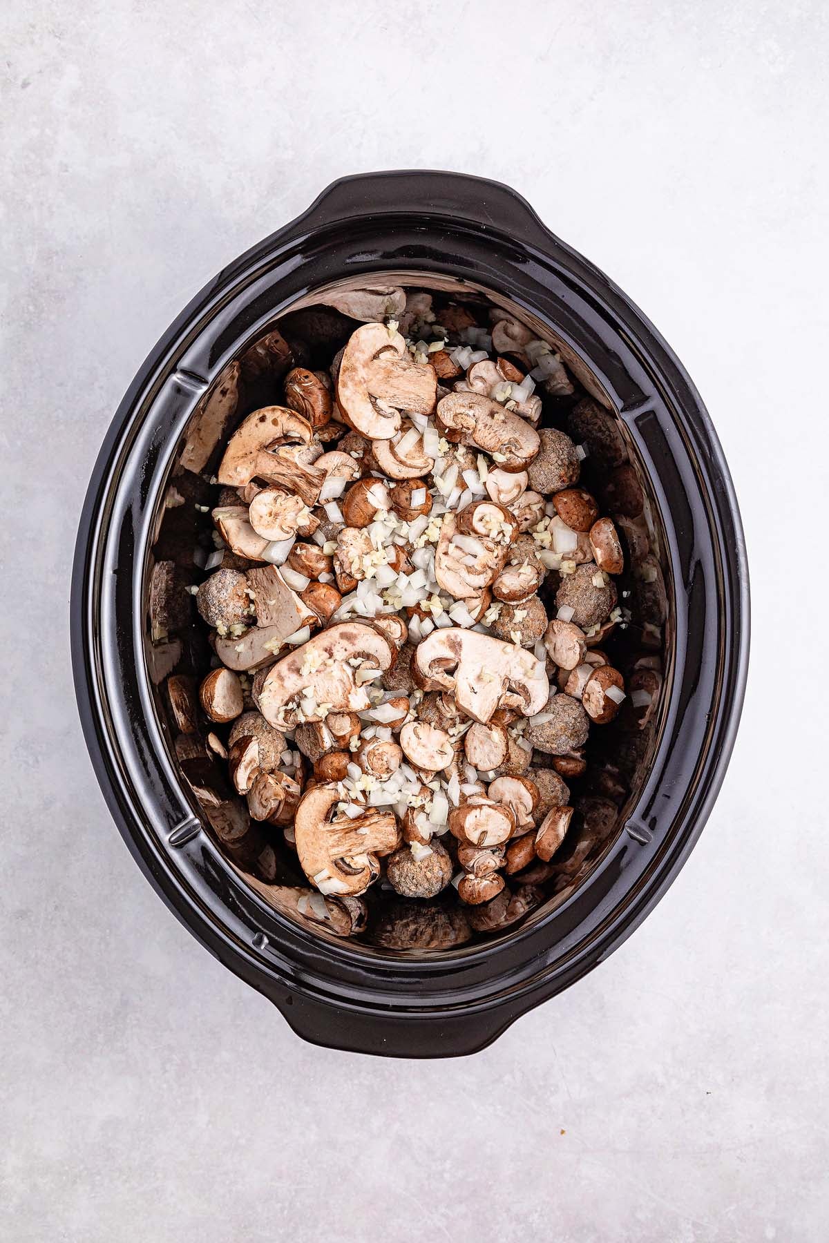 Top view of a slow cooker filled with sliced mushrooms and diced onions, creating the perfect base for flavorful Salisbury steak meatballs.