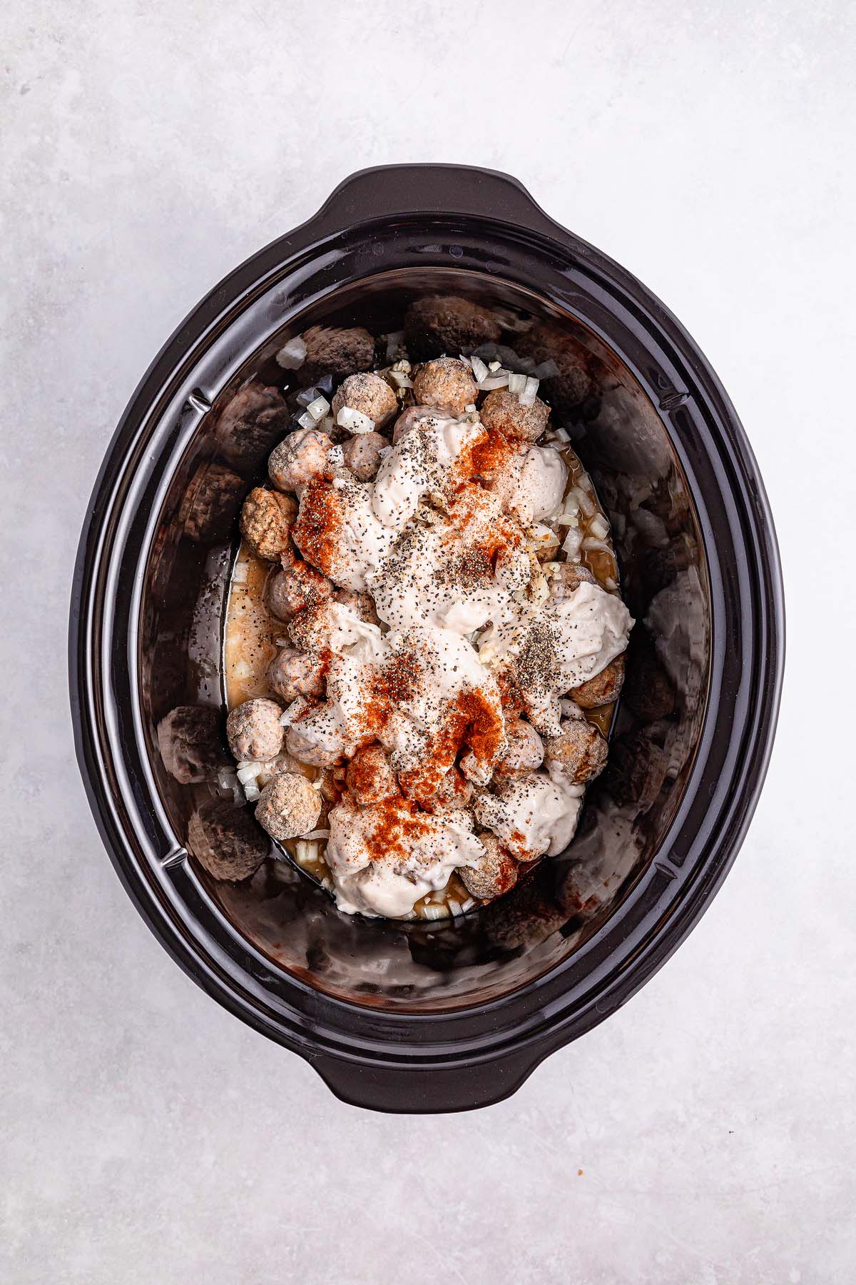 A slow cooker filled with savory delights like Swedish meatballs, flavorful seasoning, and a creamy sauce mixture.