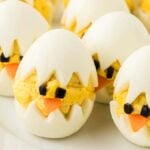 Deviled egg chicks are crafted by arranging the eggs to resemble baby chicks, using egg whites as shells. The filling forms the bodies, with tiny carrot beaks and olive eyes completing these adorable creations.