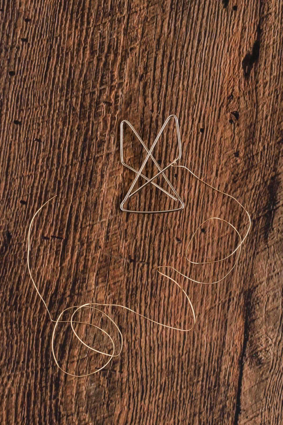 A diamond-shaped paperclip with a long string attached lies on a textured wooden surface.