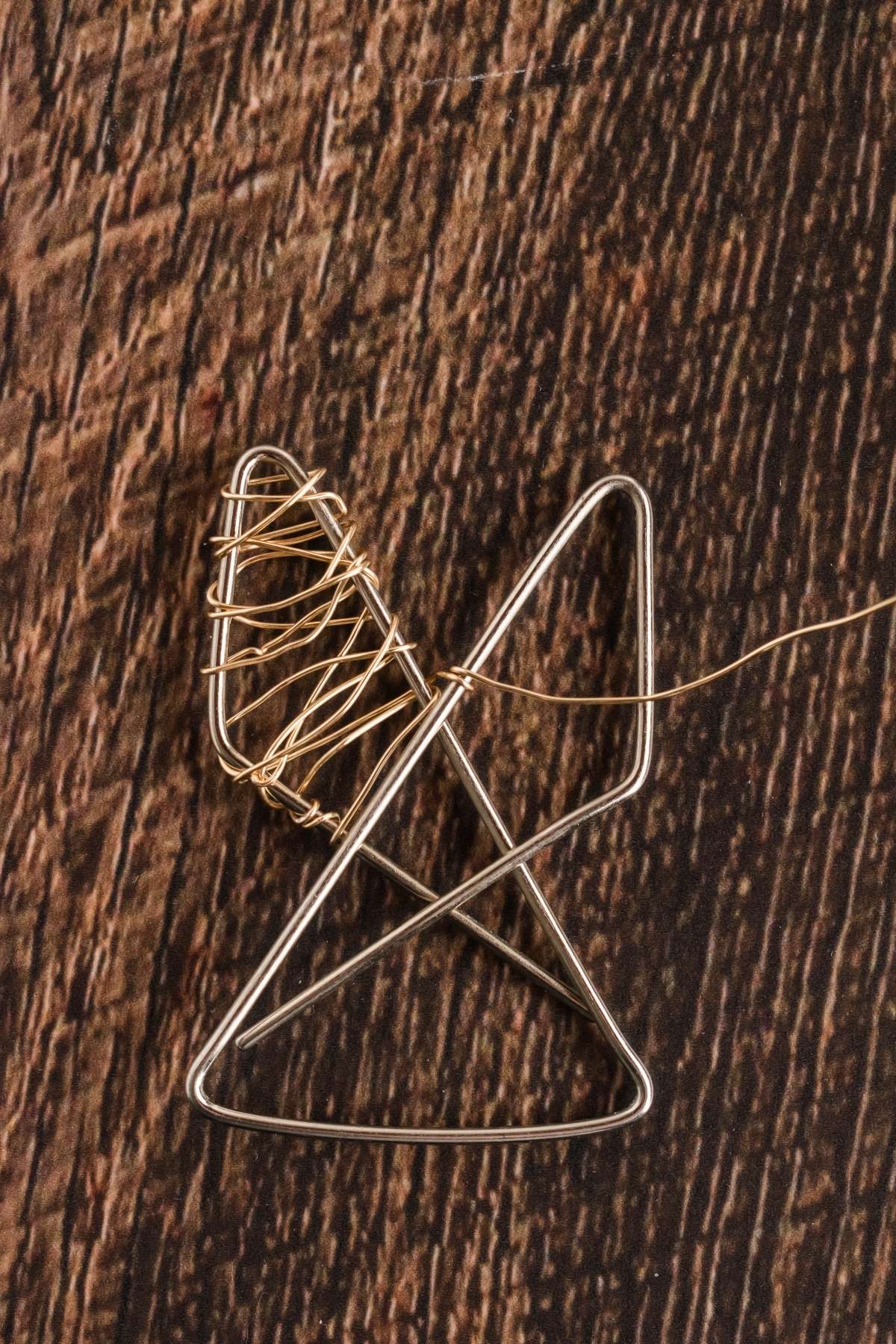Two triangular metal wire shapes intertwined, with one partially wrapped in thin wire, placed on a textured wooden surface.