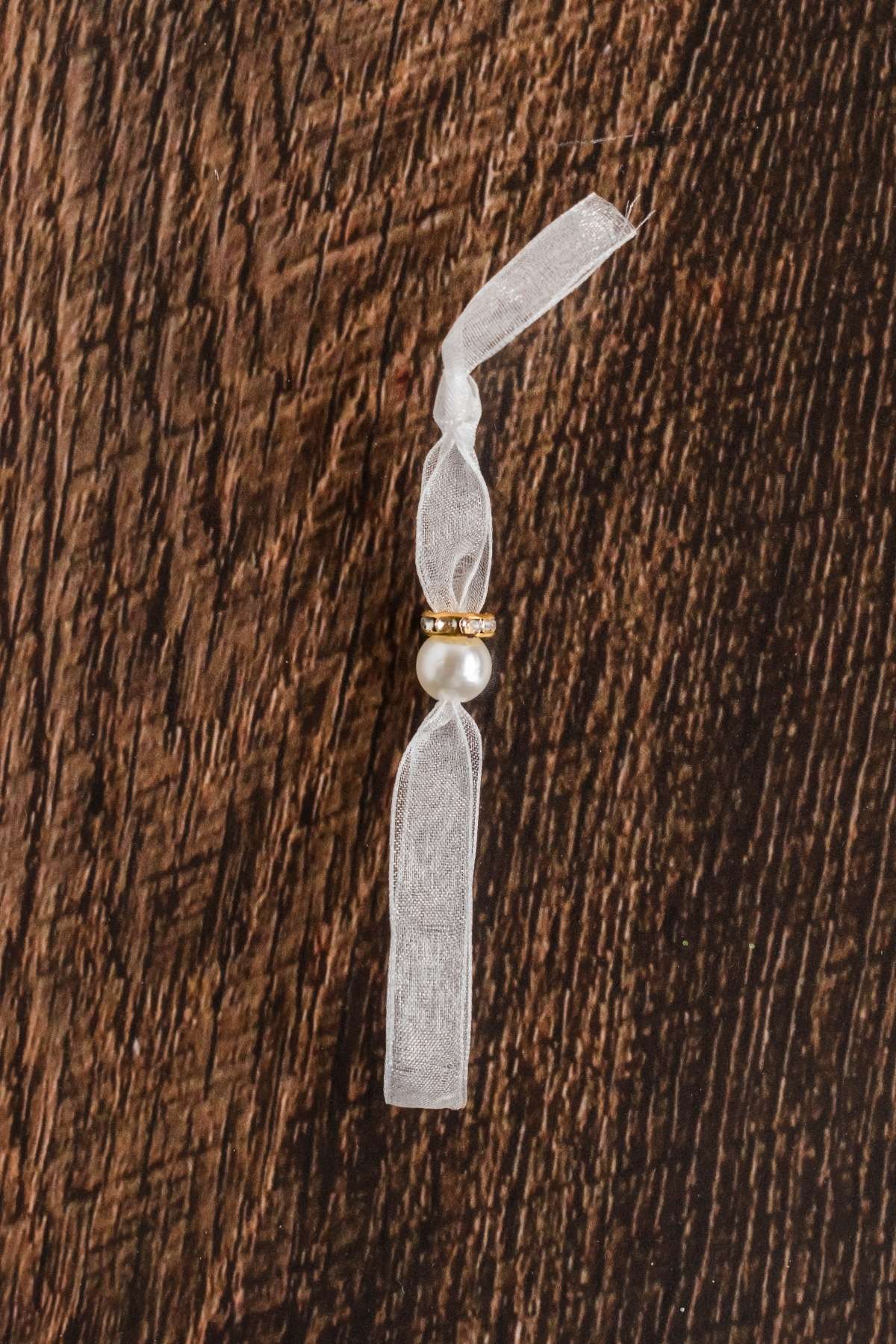 A white hair tie with a gold bead and faux pearl on a wooden surface.