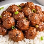 A plate of rice topped with slow cooker Asian meatballs, garnished with green onions and sesame seeds, with a fork on the side.