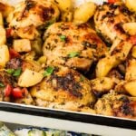 Baked Italian chicken with potatoes in a dish, garnished with herbs and red pepper pieces.