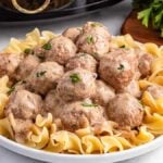 A plate of creamy slow cooker Swedish meatballs served on egg noodles, garnished with parsley.