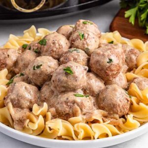 A plate of creamy slow cooker Swedish meatballs served on egg noodles, garnished with parsley.