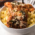 Bowl of fusilli pasta topped with saucy chicken and grated cheese on a marble surface with a striped cloth.