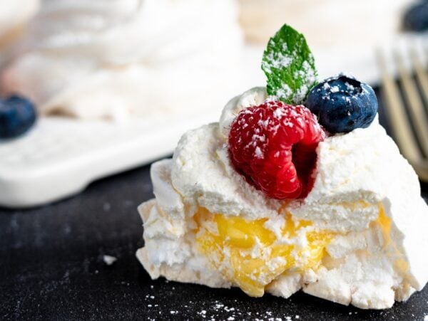 A pavlova with cream, raspberries, blueberries, and a mint leaf, dusted with powdered sugar.