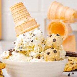 Vanilla no churn cookie dough ice cream in a bowl with a tipped cone, rich chocolate chip cookie dough, and chocolate chip cookies.