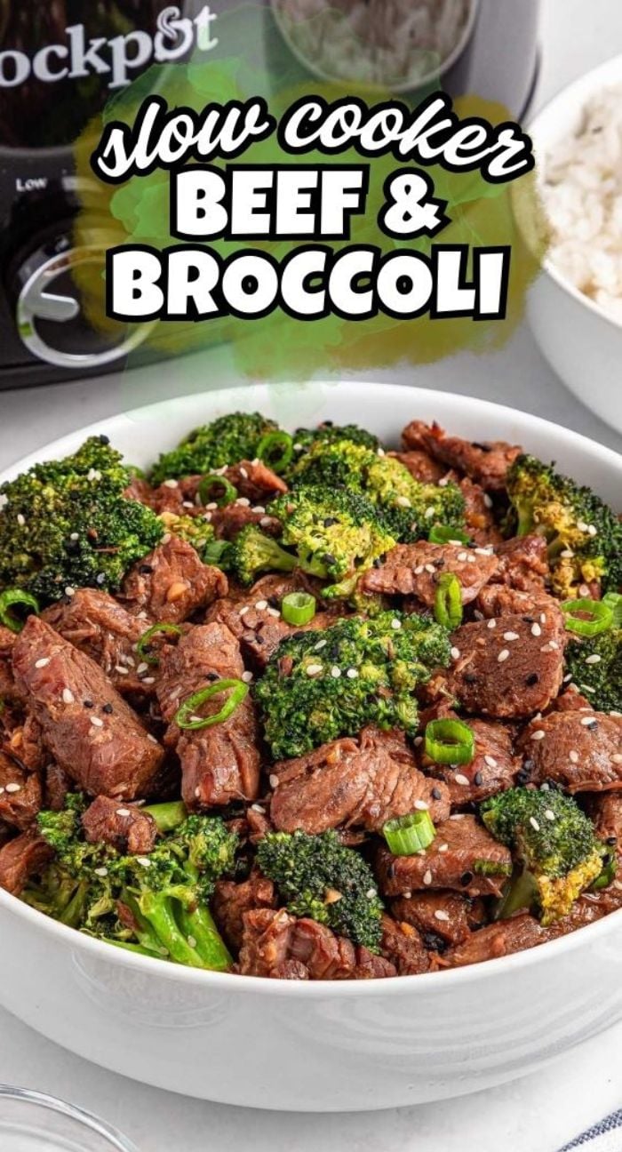 A bowl of slow cooker beef and broccoli garnished with green onions and sesame seeds sits in front of a slow cooker in the background.