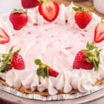 Indulge in the delightful Strawberry Cool Whip Pie, featuring a creamy pink filling and topped with luscious whipped topping and fresh strawberries, all nestled on a classic graham cracker crust.