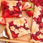A delightful strawberry slab pie graces the baking tray, its decorative flower crust perfectly baked. Fresh strawberries accompany a gleaming serving spatula, inviting you to indulge in this artistic and delicious creation.