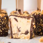 Indulge in our homemade Peanut Buster Bars: creamy vanilla ice cream on wooden sticks, perfectly coated with rich chocolate and crunchy nuts. One bar is partially eaten, revealing the velvety treat inside.