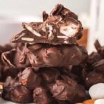 Close-up of stacked rocky road bites featuring chocolate almond clusters with visible nuts and marshmallows, surrounded by scattered nuts and marshmallows.