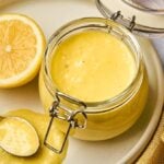 Jar of whole lemon vinaigrette on a plate with a halved lemon and spoon.