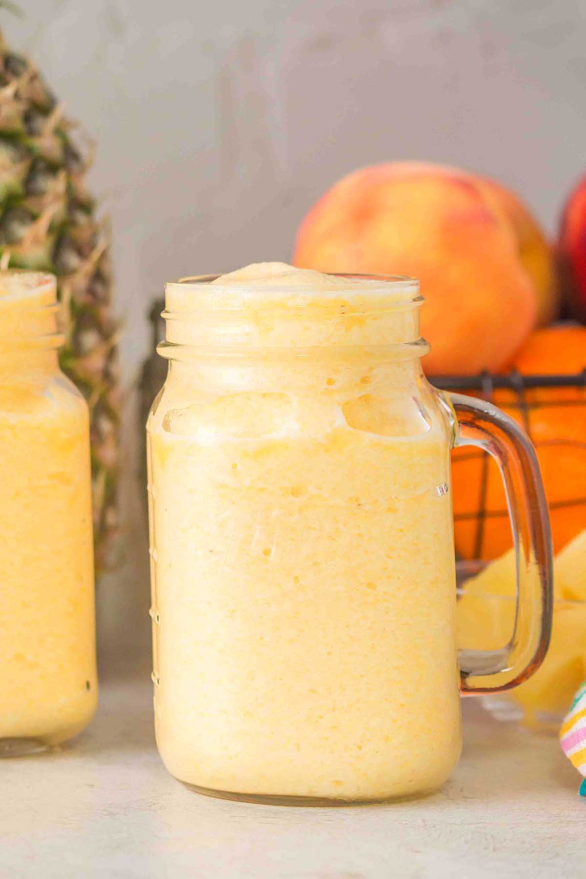 Frosty Pineapple Peach Smoothie in a mason jar, with fresh fruit in the background.