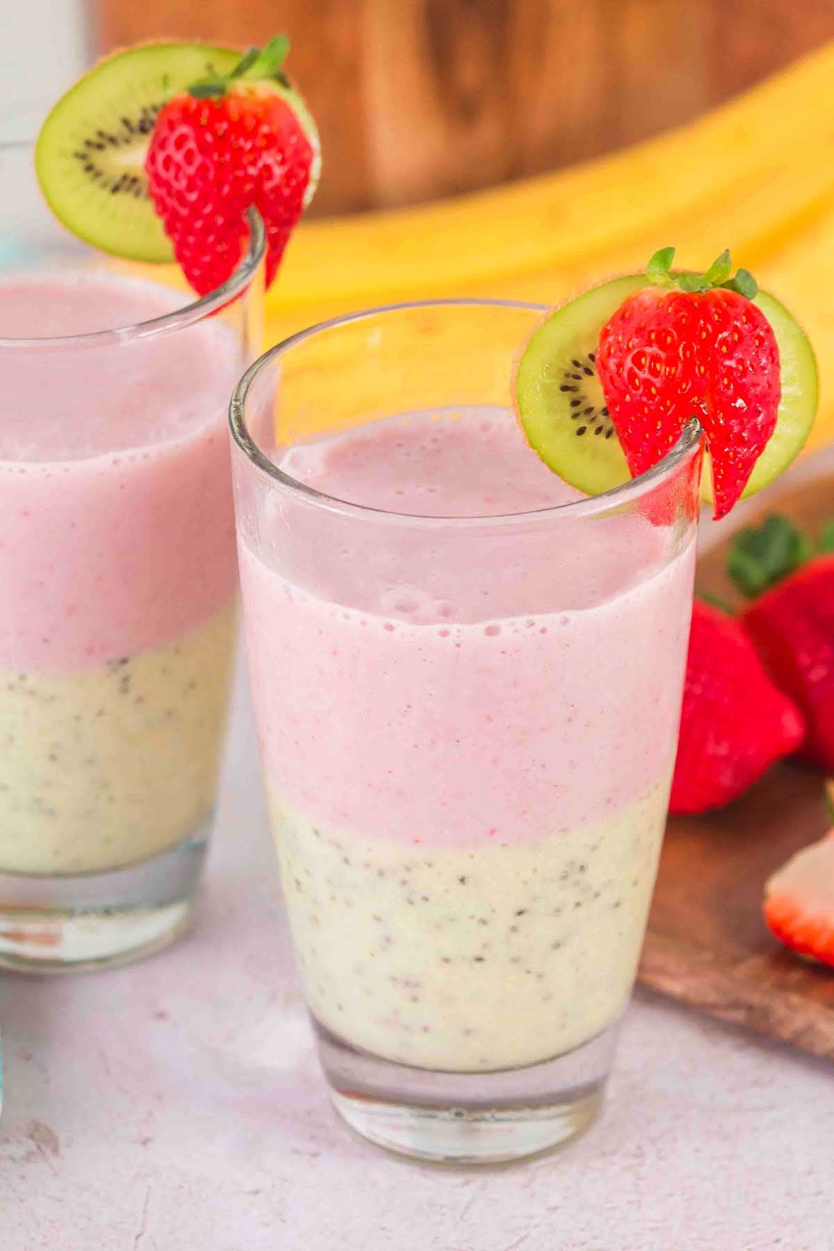 Layered Kiwi Strawberry Smoothie served in glasses, showcasing two vibrant layers and topped with fresh strawberry and kiwi slices as garnish.