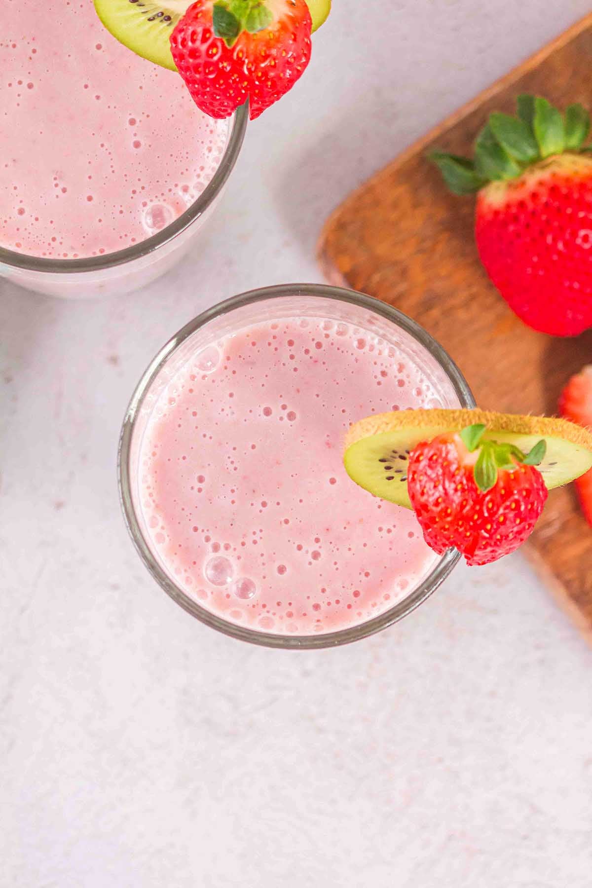 Layered Kiwi Strawberry Smoothie served in a glass, garnished with a strawberry and kiwi slice, sits beside fresh strawberries.