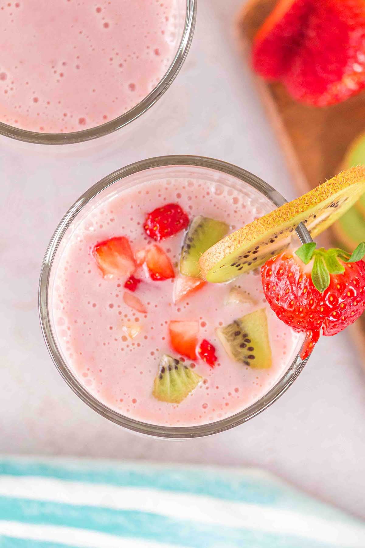 Glass of Layered Kiwi Strawberry Smoothie, topped with vibrant kiwi and strawberry slices, viewed from above.