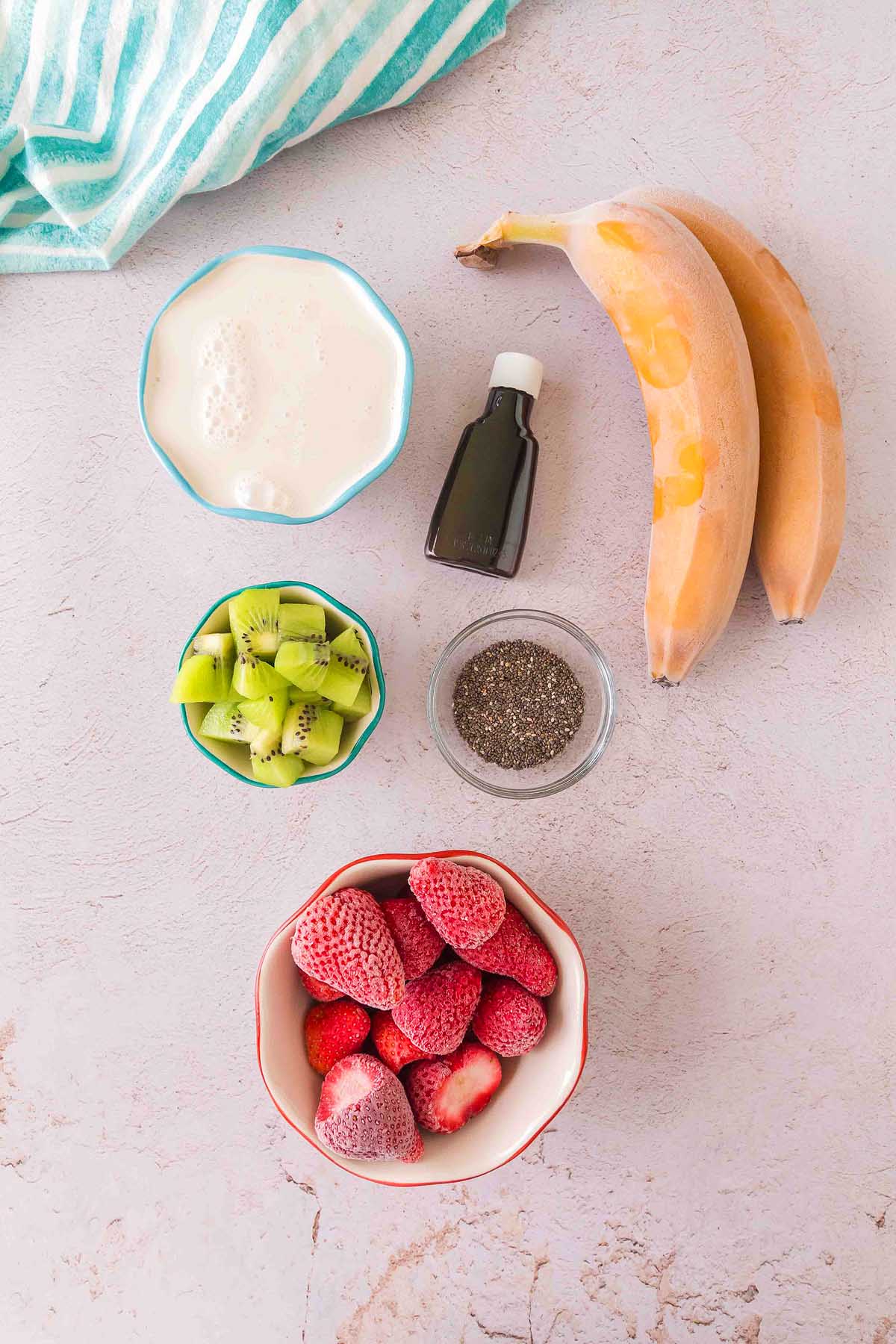 Layered Kiwi Strawberry Smoothie featuring bananas, strawberries, kiwi, chia seeds, yogurt, and vanilla extract arranged on a light surface.