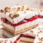 A slice of cherry lush dessert with whipped cream, cherry filling, and nuts on a graham cracker crust.