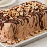 A Chocolate Hazelnut Semifreddo ice cream loaf topped with chopped nuts and drizzled with chocolate, served on a metal tray.