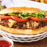 A Chopped Cheese Sandwich with ground beef, melted cheese, tomato slices, and lettuce on a plate, served with ketchup and mustard nearby.