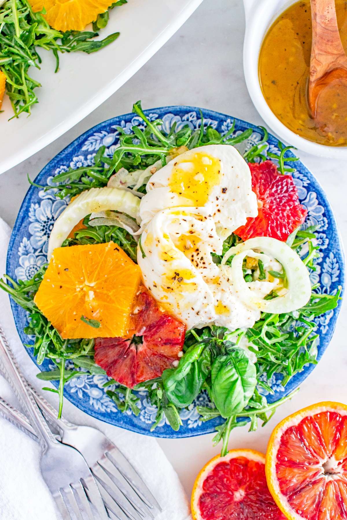 Salad with arugula, fennel, orange, and blood orange slices, topped with buffalo mozzarella and dressing on the side.