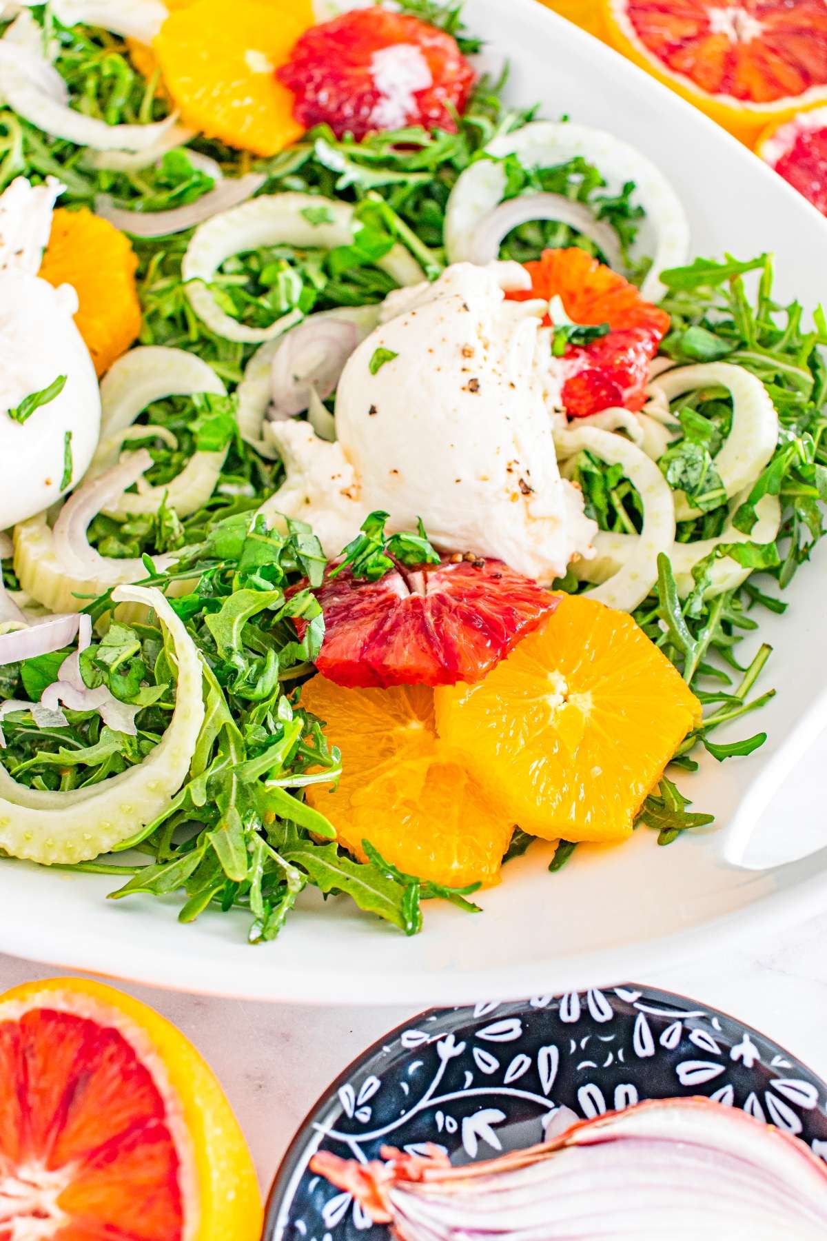 Salad with arugula, fennel, blood orange slices, and mozzarella on a white plate.