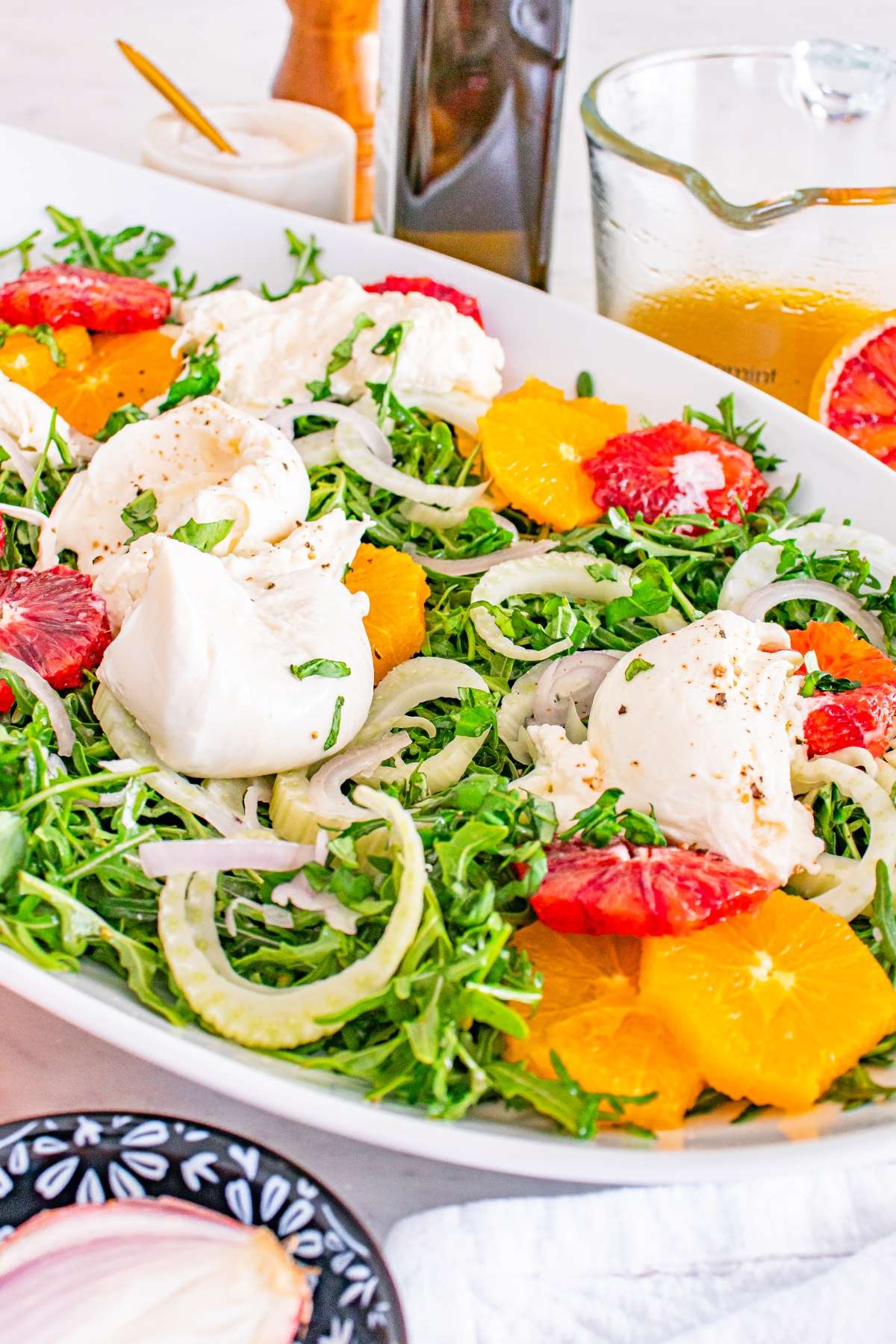 Fresh salad with arugula, oranges, fennel, burrata, and citrus dressing in a white bowl.