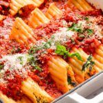 Baked manicotti pasta with tomato sauce, cheese, and herbs in a white dish.