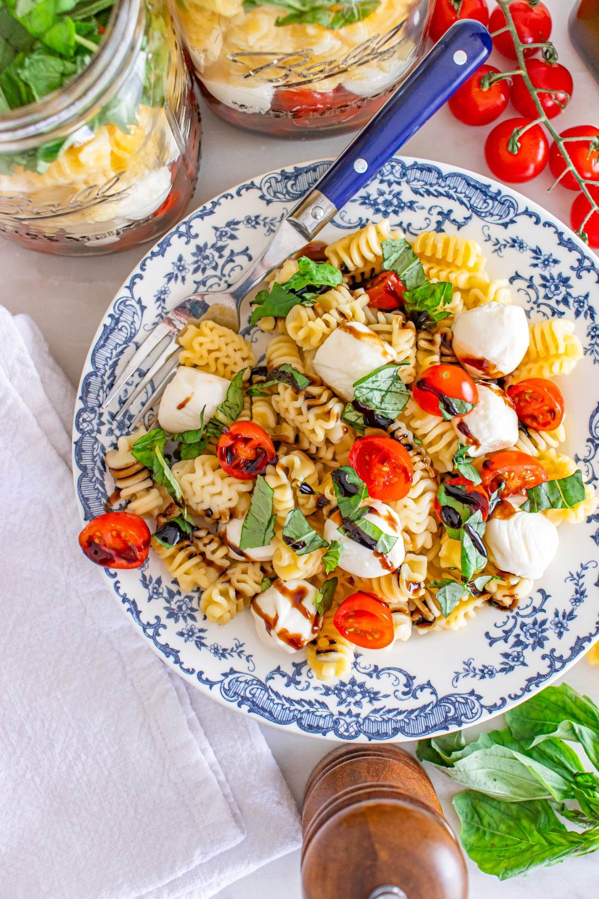 Pasta salad with cherry tomatoes, mozzarella, basil, and balsamic glaze on a blue and white plate.
