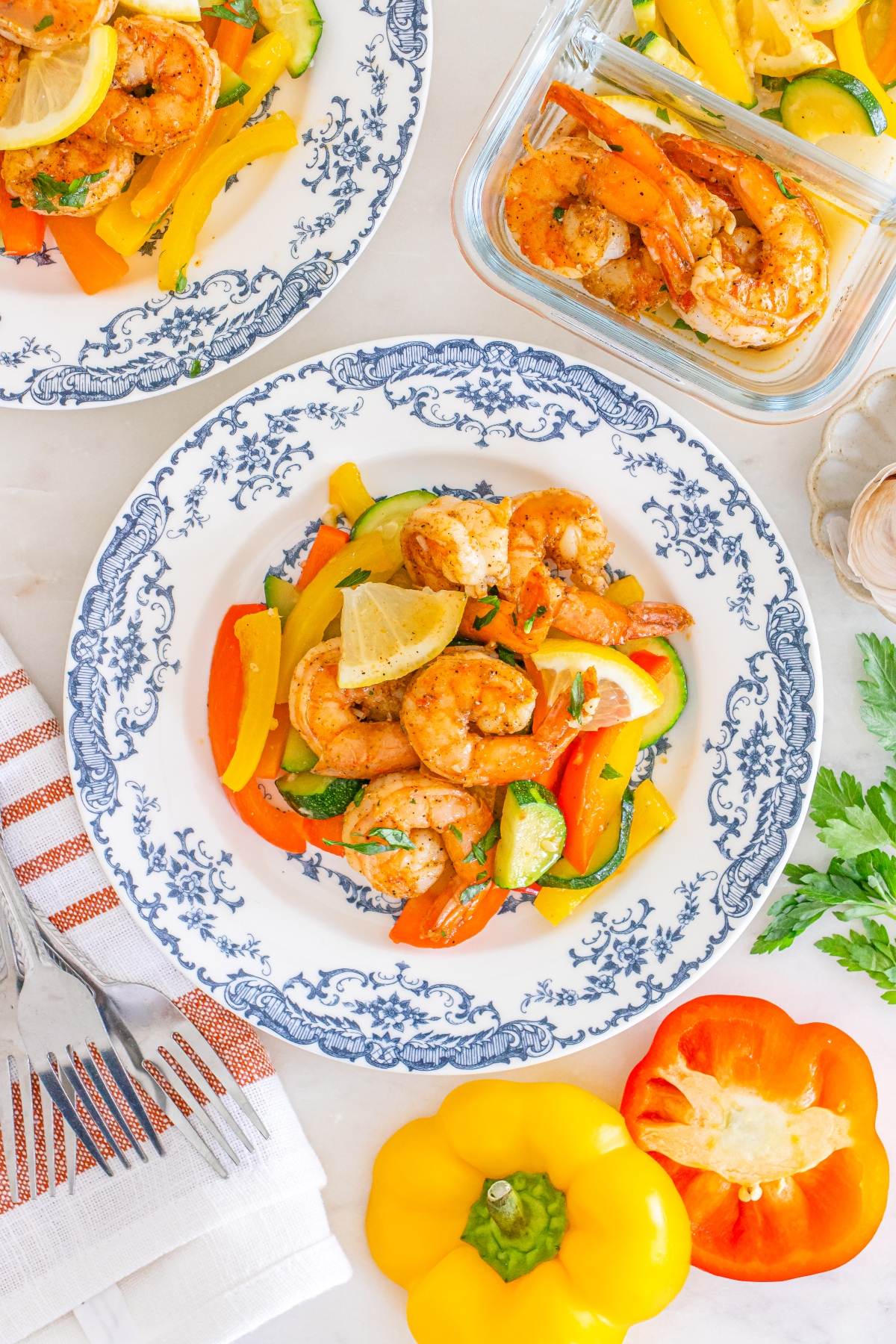 Blue and white plates with shrimp, bell peppers, and zucchini, garnished with lemon slices and parsley.