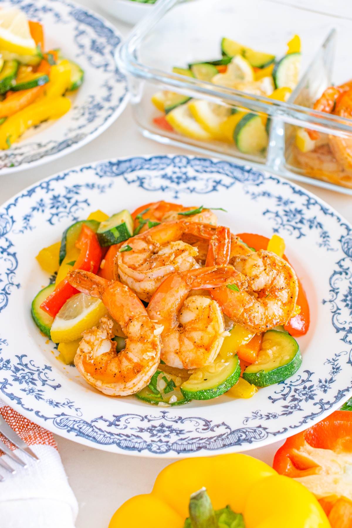 Shrimp and sautéed vegetables served on a decorative plate, with extra veggies and shrimp in the background.