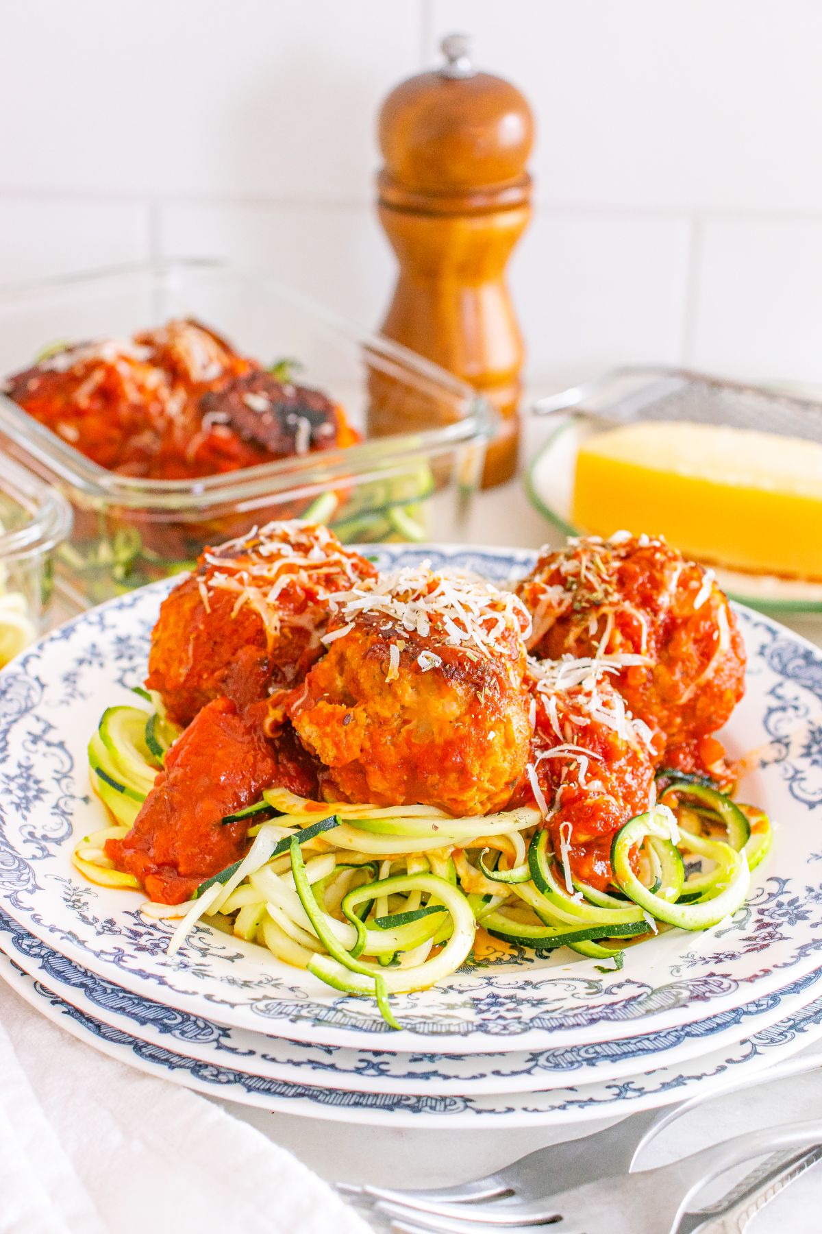 Meal Prep Turkey Meatballs & Zoodles in tomato sauce are served over spiralized zucchini noodles on a patterned plate, finished with a sprinkle of grated cheese.