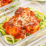 Glass containers filled with Meal Prep Turkey Meatballs & Zoodles, topped with rich tomato sauce and a sprinkle of grated cheese.